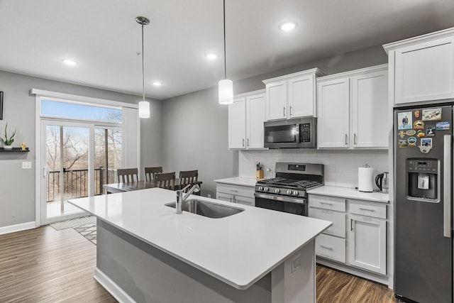 kitchen featuring backsplash, white cabinets, a center island with sink, sink, and appliances with stainless steel finishes