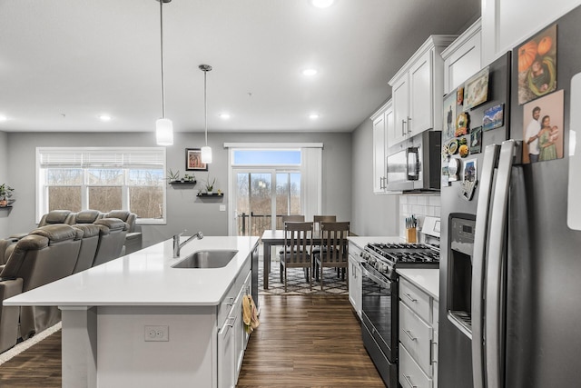 kitchen with appliances with stainless steel finishes, sink, white cabinets, hanging light fixtures, and an island with sink