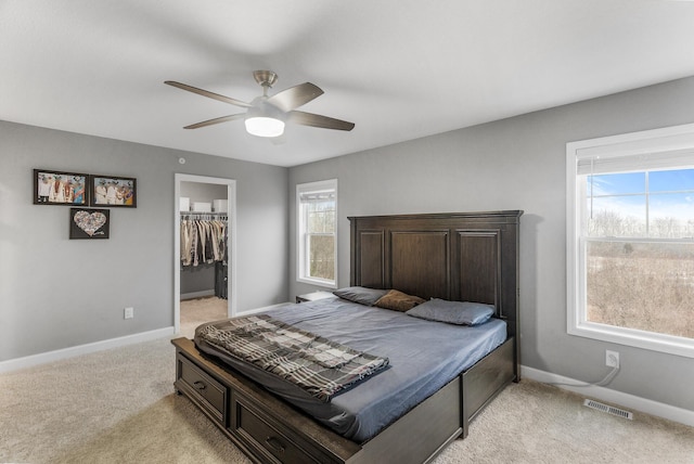 bedroom with a closet, a spacious closet, ceiling fan, and light colored carpet