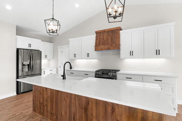 kitchen featuring high end black range oven, stainless steel fridge with ice dispenser, decorative light fixtures, and a kitchen island with sink