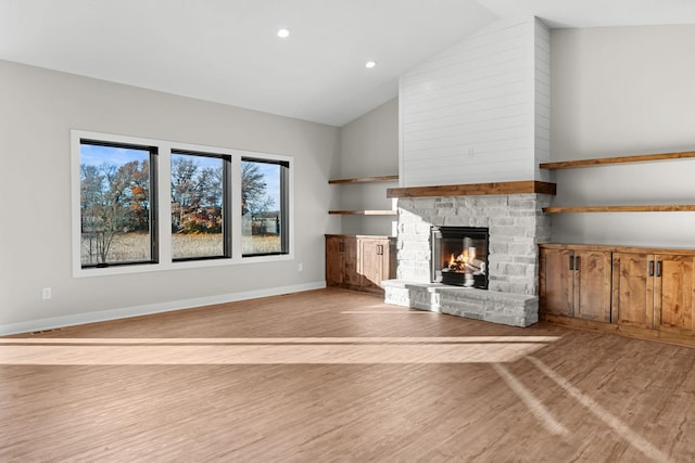 unfurnished living room with a wealth of natural light, a fireplace, vaulted ceiling, and light wood-type flooring