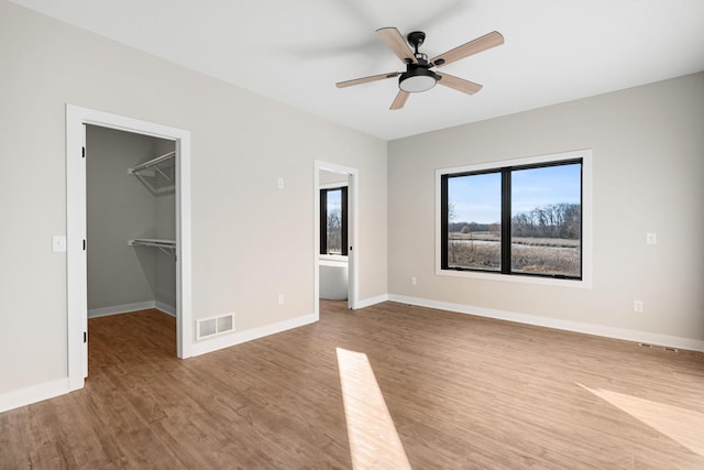 unfurnished bedroom featuring ceiling fan, a spacious closet, light hardwood / wood-style flooring, and a closet