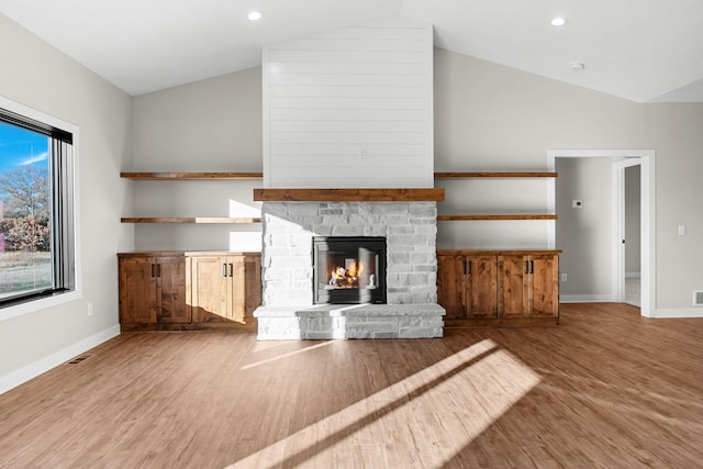 unfurnished living room featuring a stone fireplace, lofted ceiling, and wood-type flooring