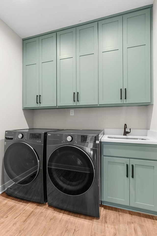 laundry room with cabinets, light wood-type flooring, sink, and washing machine and dryer