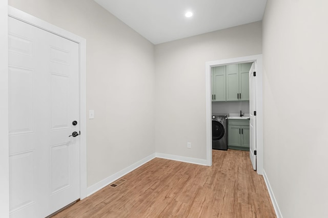 clothes washing area featuring washer / clothes dryer, light hardwood / wood-style flooring, cabinets, and sink