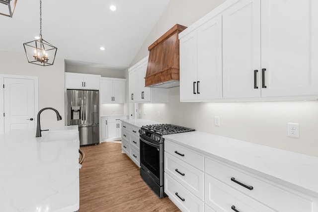 kitchen featuring white cabinetry, light stone counters, pendant lighting, vaulted ceiling, and appliances with stainless steel finishes