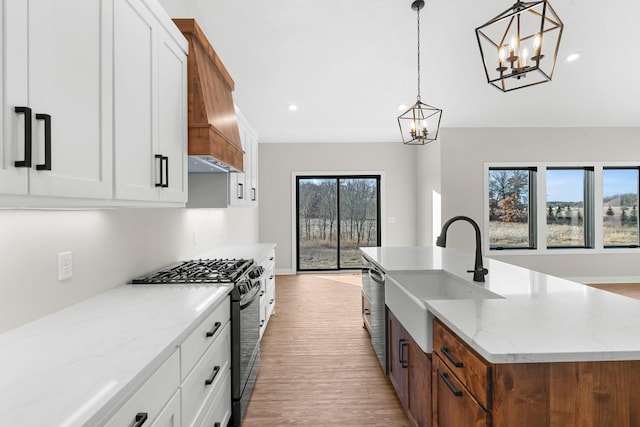 kitchen with white cabinetry, sink, hanging light fixtures, stainless steel appliances, and an island with sink