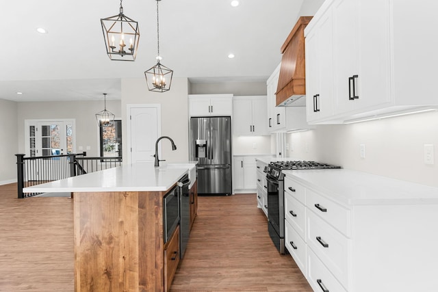 kitchen featuring gas stove, stainless steel fridge, an island with sink, decorative light fixtures, and white cabinets