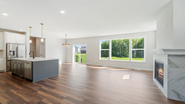 kitchen with white cabinets, a center island with sink, a premium fireplace, decorative light fixtures, and stainless steel appliances