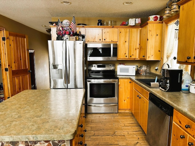 kitchen featuring a textured ceiling, appliances with stainless steel finishes, light hardwood / wood-style flooring, and a center island