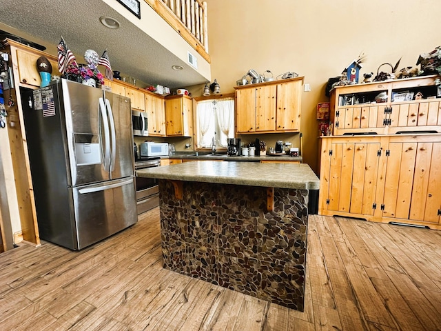 kitchen featuring a textured ceiling, appliances with stainless steel finishes, a kitchen island, and light wood-type flooring