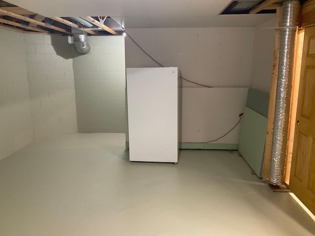 unfinished below grade area featuring concrete block wall and freestanding refrigerator