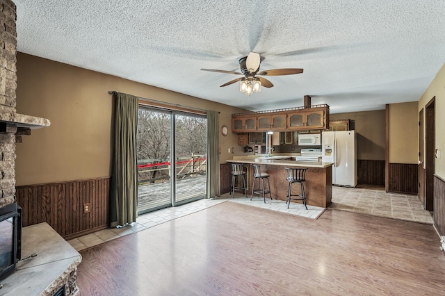 kitchen with ceiling fan, kitchen peninsula, white appliances, a breakfast bar area, and a fireplace