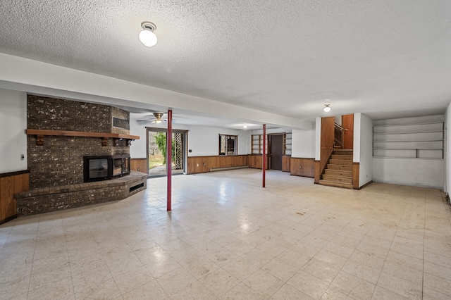 basement featuring wood walls, ceiling fan, a textured ceiling, baseboard heating, and a fireplace