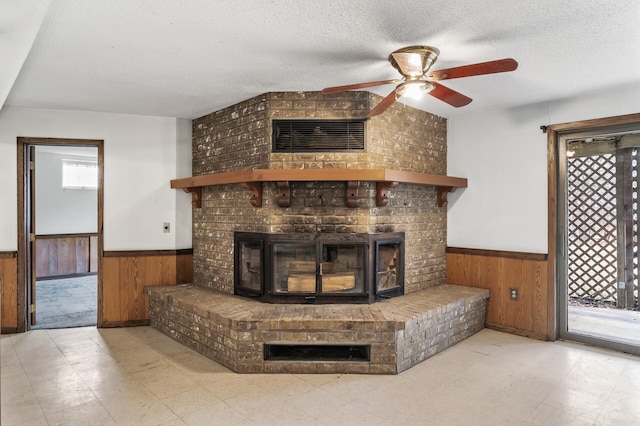 room details with wooden walls, ceiling fan, a textured ceiling, and a brick fireplace