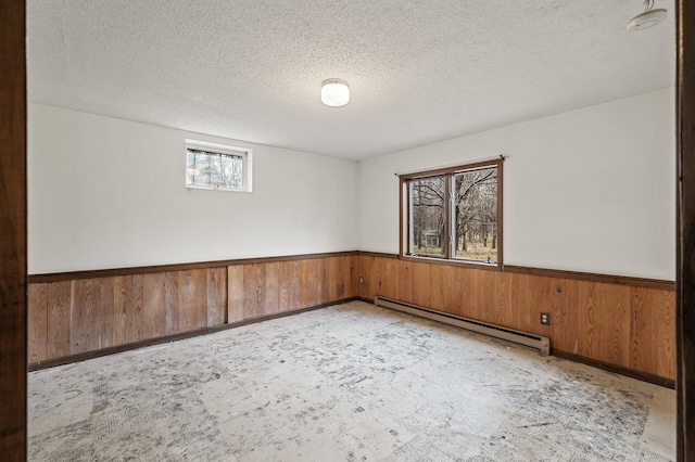 spare room featuring a textured ceiling, a baseboard heating unit, and wood walls