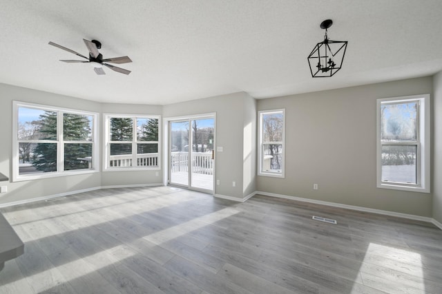 empty room featuring ceiling fan with notable chandelier, a textured ceiling, and light hardwood / wood-style flooring