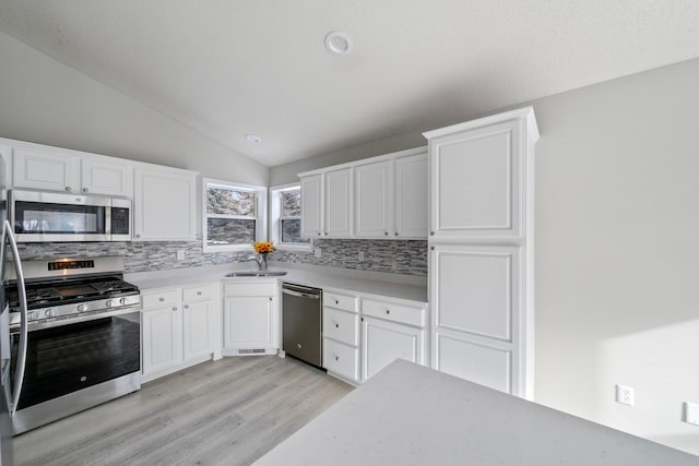 kitchen featuring decorative backsplash, white cabinets, stainless steel appliances, and vaulted ceiling