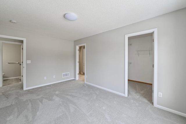 unfurnished bedroom featuring a spacious closet, connected bathroom, a closet, light colored carpet, and a textured ceiling