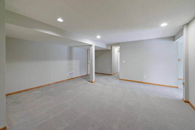 basement featuring light colored carpet and a textured ceiling