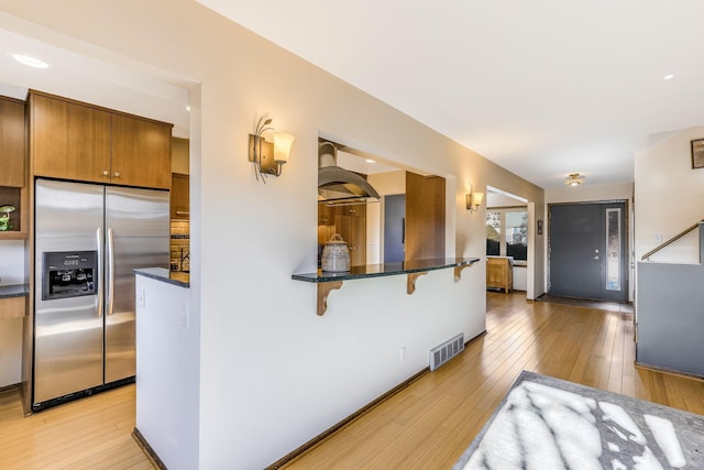 kitchen featuring stainless steel fridge with ice dispenser, light hardwood / wood-style flooring, and a kitchen breakfast bar