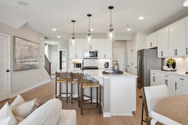 kitchen featuring white cabinets, appliances with stainless steel finishes, pendant lighting, and an island with sink