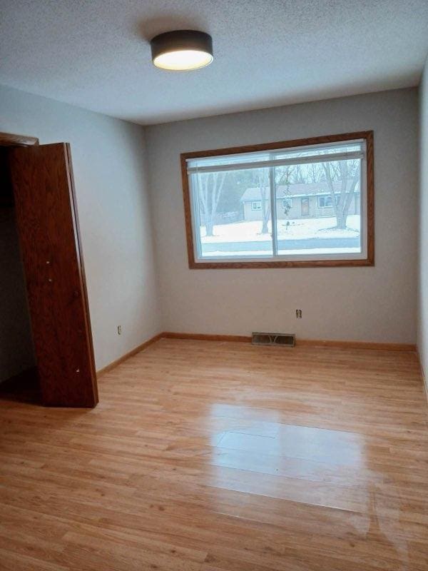 unfurnished room with light wood-style floors, baseboards, visible vents, and a textured ceiling