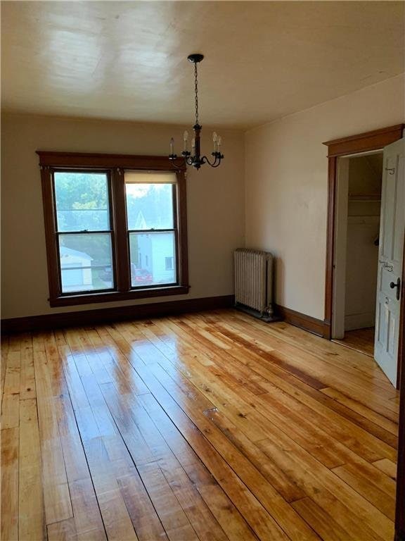 unfurnished dining area with radiator, a notable chandelier, and light wood-type flooring