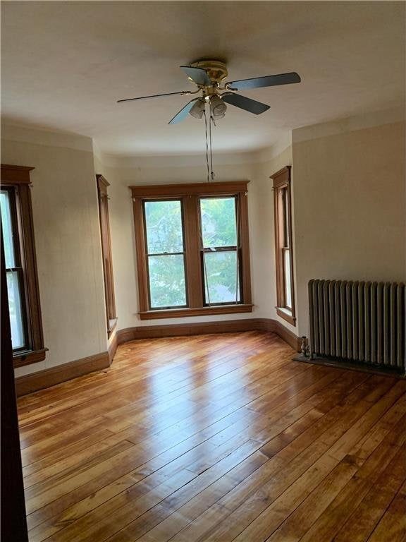 empty room featuring light hardwood / wood-style floors, radiator heating unit, crown molding, and ceiling fan