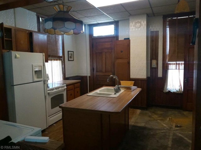 kitchen featuring wood walls, sink, white appliances, a paneled ceiling, and an island with sink