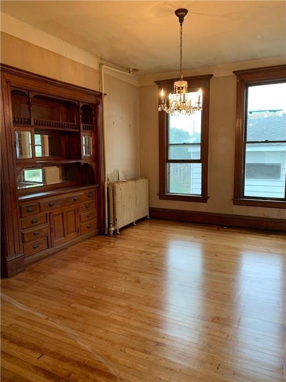 unfurnished dining area featuring an inviting chandelier, light hardwood / wood-style floors, and radiator heating unit