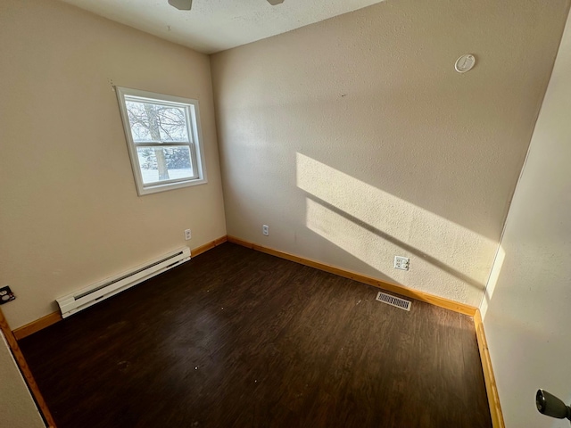 empty room featuring ceiling fan, dark wood-type flooring, and a baseboard heating unit