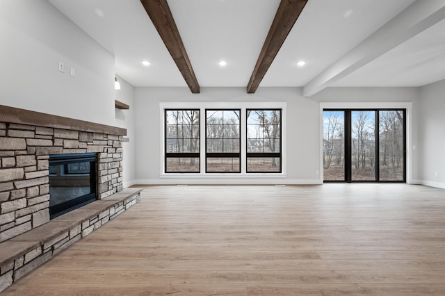 unfurnished living room featuring beamed ceiling, light hardwood / wood-style floors, and a stone fireplace