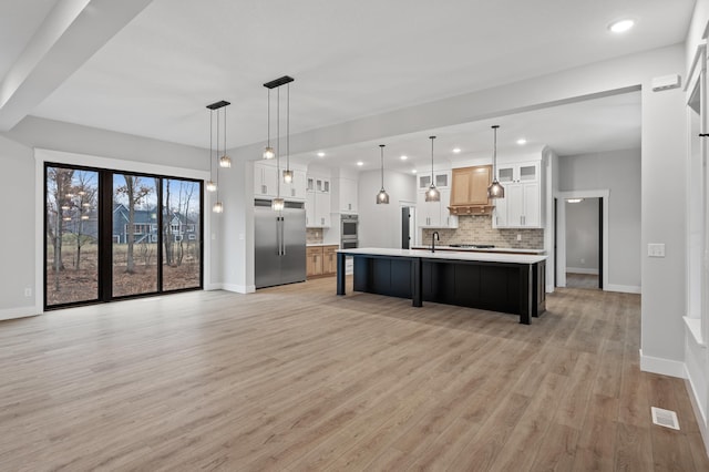 kitchen with appliances with stainless steel finishes, tasteful backsplash, a kitchen island with sink, decorative light fixtures, and white cabinetry