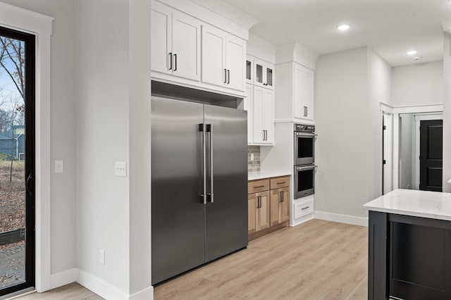 kitchen with appliances with stainless steel finishes, light wood-type flooring, tasteful backsplash, light stone counters, and white cabinetry