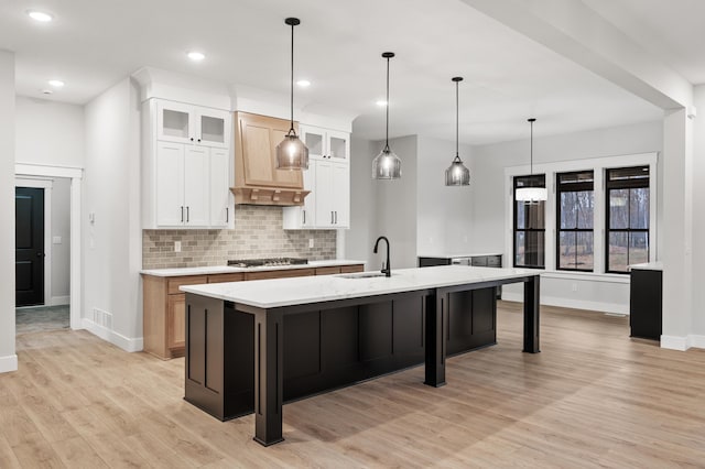 kitchen with decorative backsplash, a kitchen island with sink, sink, light hardwood / wood-style flooring, and white cabinetry