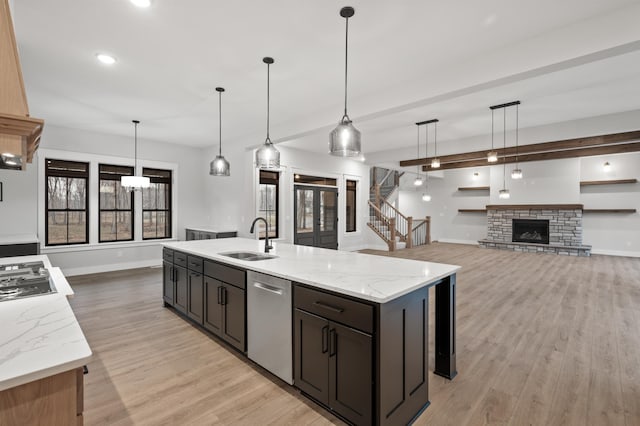 kitchen featuring sink, hanging light fixtures, light stone counters, an island with sink, and appliances with stainless steel finishes