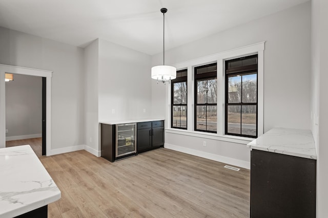 interior space with pendant lighting, light hardwood / wood-style flooring, beverage cooler, and light stone counters