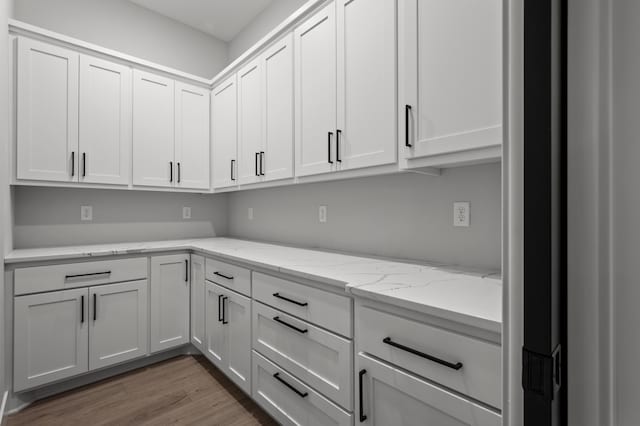 kitchen featuring white cabinets, light stone countertops, and hardwood / wood-style flooring