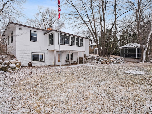 snow covered house featuring a sunroom and a storage unit