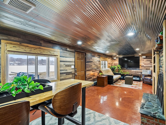 dining room with concrete floors, a water view, wooden walls, and wood ceiling