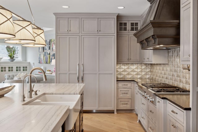 kitchen featuring light hardwood / wood-style flooring, stainless steel gas stovetop, custom range hood, decorative light fixtures, and decorative backsplash