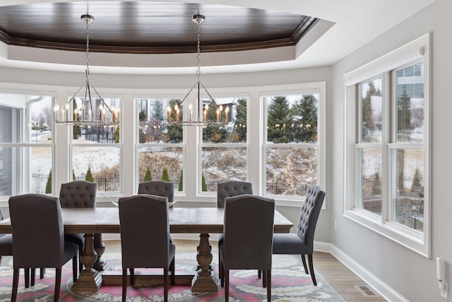 dining space with wood-type flooring, ornamental molding, a chandelier, and a raised ceiling