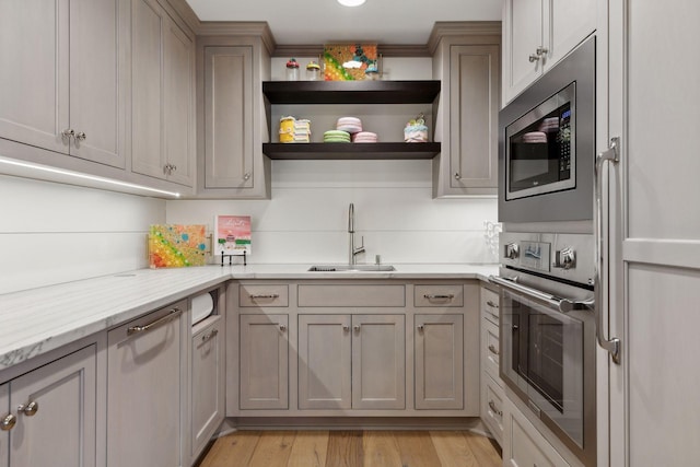 kitchen featuring gray cabinetry, sink, light hardwood / wood-style flooring, stainless steel appliances, and light stone counters