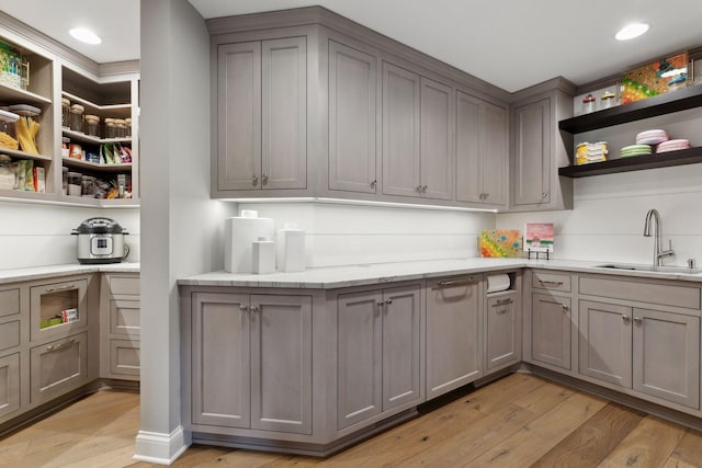 kitchen with light stone countertops, sink, gray cabinetry, and light hardwood / wood-style flooring