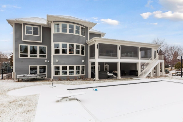 snow covered rear of property featuring a sunroom