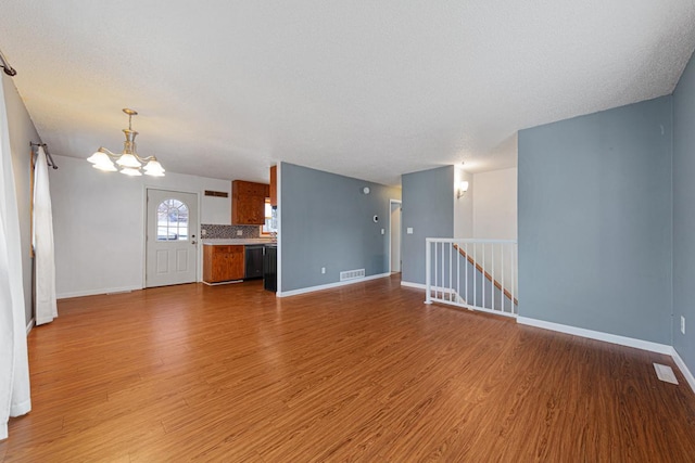 unfurnished living room with light wood-type flooring, a textured ceiling, and a notable chandelier