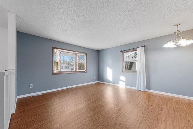 spare room with a textured ceiling, an inviting chandelier, a wealth of natural light, and hardwood / wood-style flooring