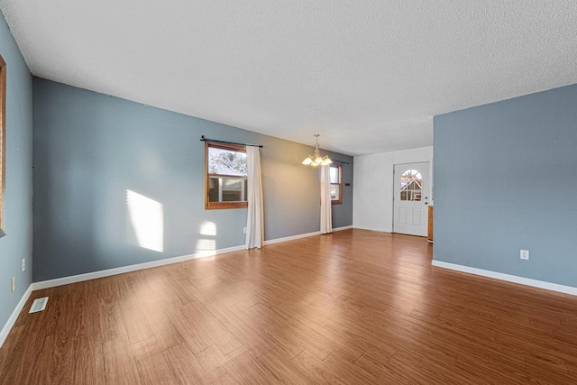 unfurnished room with a textured ceiling, wood-type flooring, and a notable chandelier