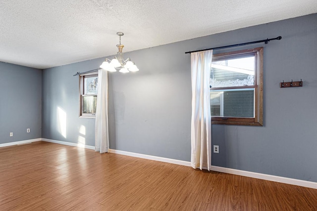 unfurnished room featuring a textured ceiling, an inviting chandelier, and wood-type flooring